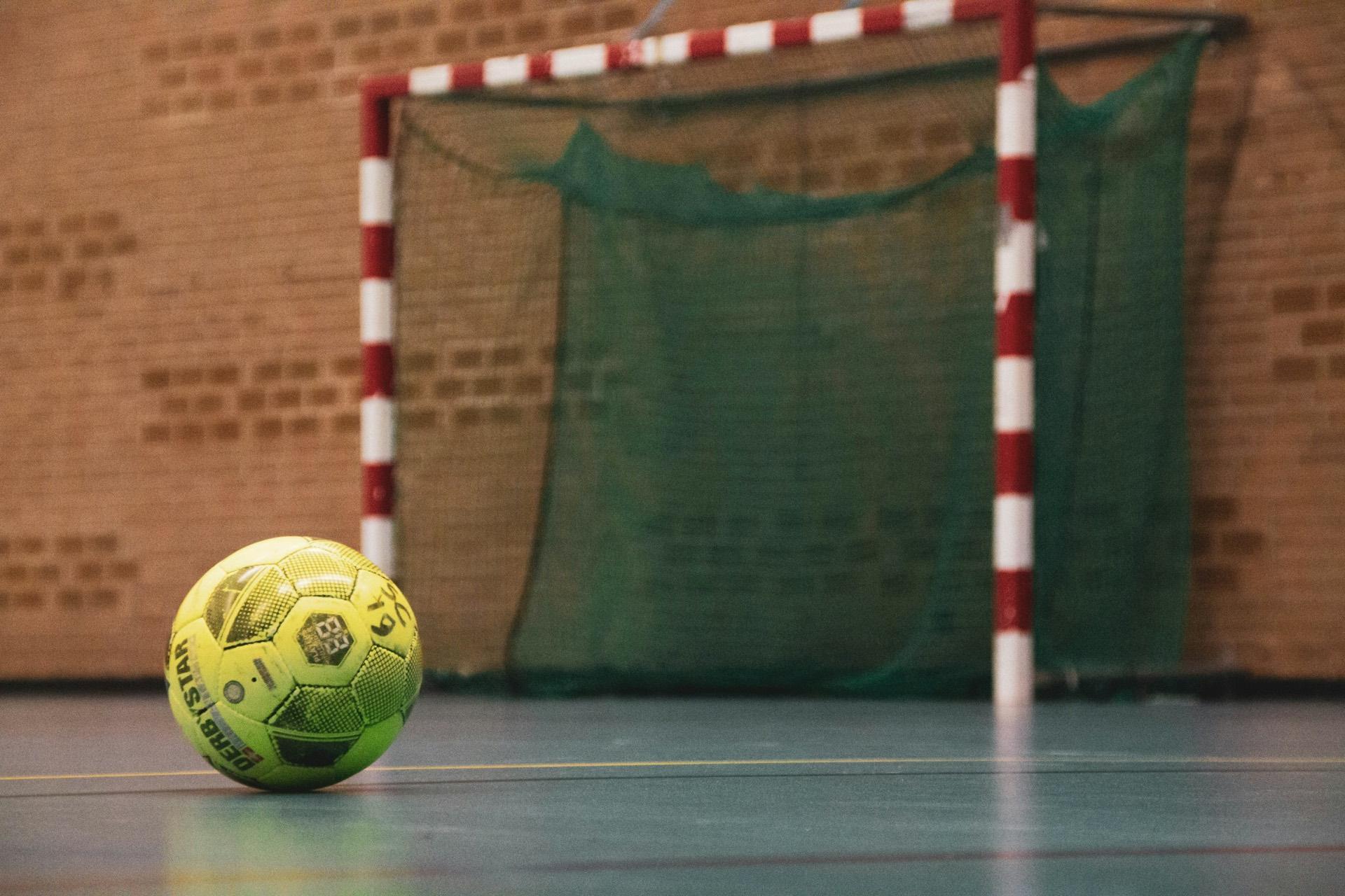 Balón amarillo sobre el piso de un gimnasio, frente a un marco de rayas rojas y blancas